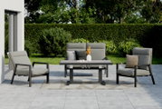 Tuinsetset met twee grijze fauteuils, een grijze tuinbank en een tafel op een terras, omgeven door een groene haag en bomen, gezien vanuit een vooraanzicht.