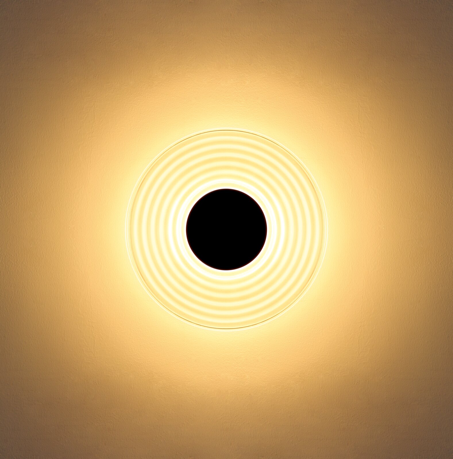 Runde Deckenleuchte mit konzentrischen Ringen und warmweißem Lichtschein an heller Decke, Ansicht von unten (Untersicht)