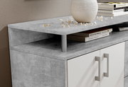 Nahaufnahme eines modernen Sideboards mit grauer Steinoptik-Oberfläche, dekoriert mit einem weißen Keramikgefäß und Büchern, aus seitlicher Perspektive.