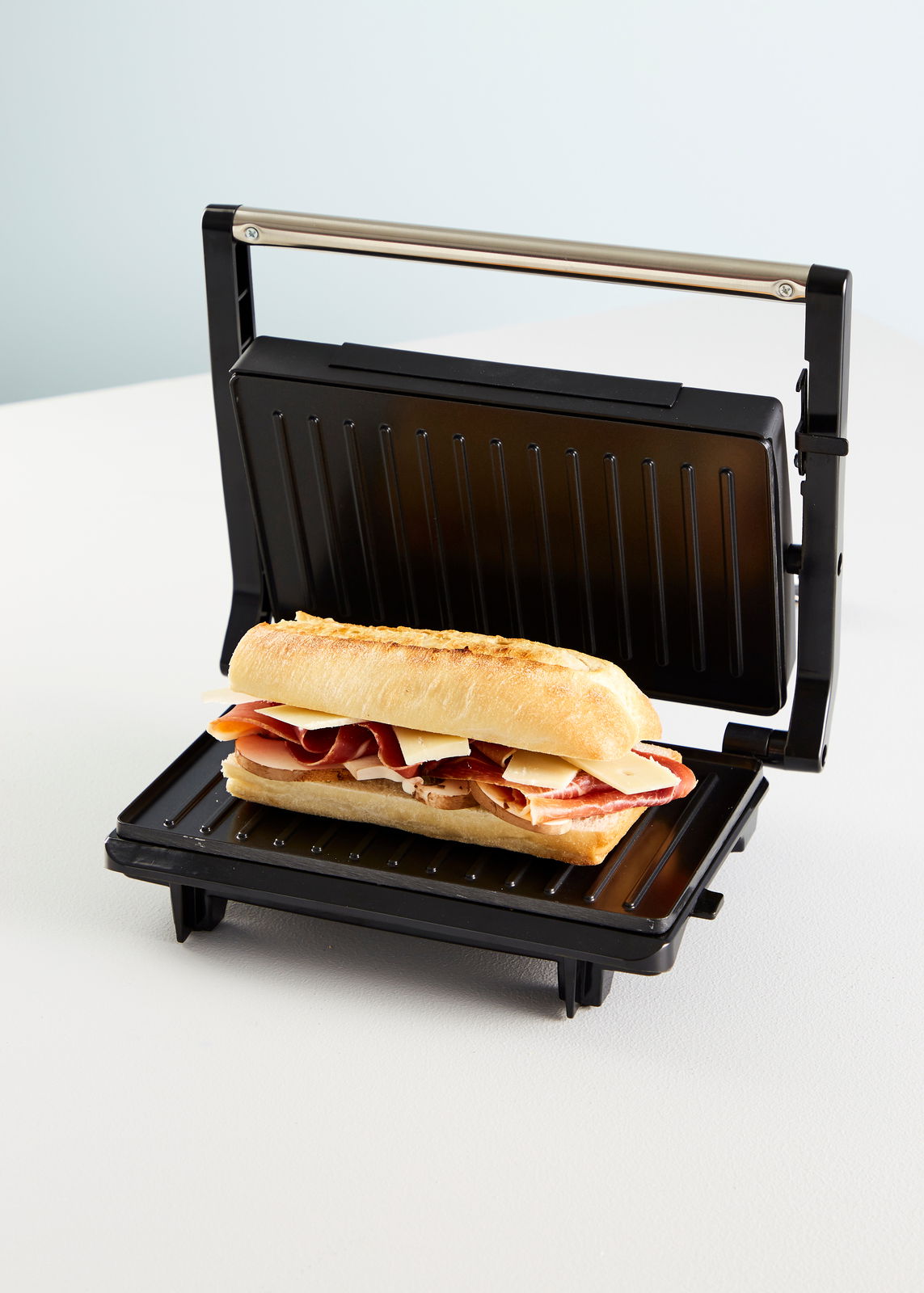 Panini Grill mit geöffnetem Deckel und einem belegten Baguette, seitliche Perspektive