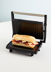 Panini Grill mit geöffnetem Deckel und einem belegten Baguette, seitliche Perspektive