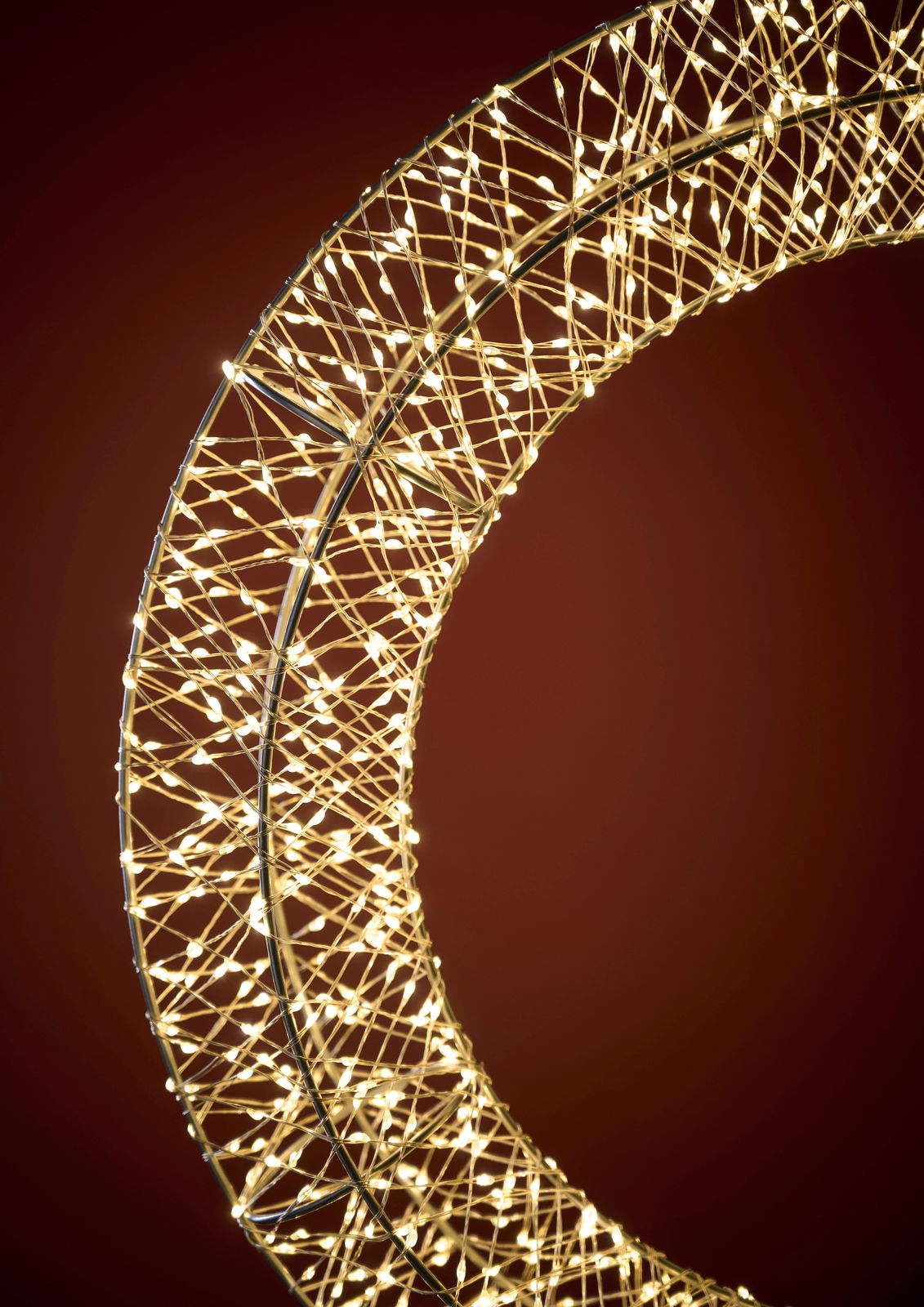 Nahaufnahme eines LED-Kranzes mit einem Durchmesser von 50 cm, der in einem warmen Licht leuchtet. Der Kranz ist aus einem filigranen Drahtgeflecht gefertigt und wird von zahlreichen kleinen LED-Lichtern erhellt. Die Perspektive zeigt den Kranz von der Se