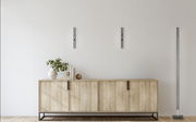 Moderne LED-Wandleuchte BEN in minimalistischem Design, frontal an einer weißen Wand über einem Holzschrank montiert.