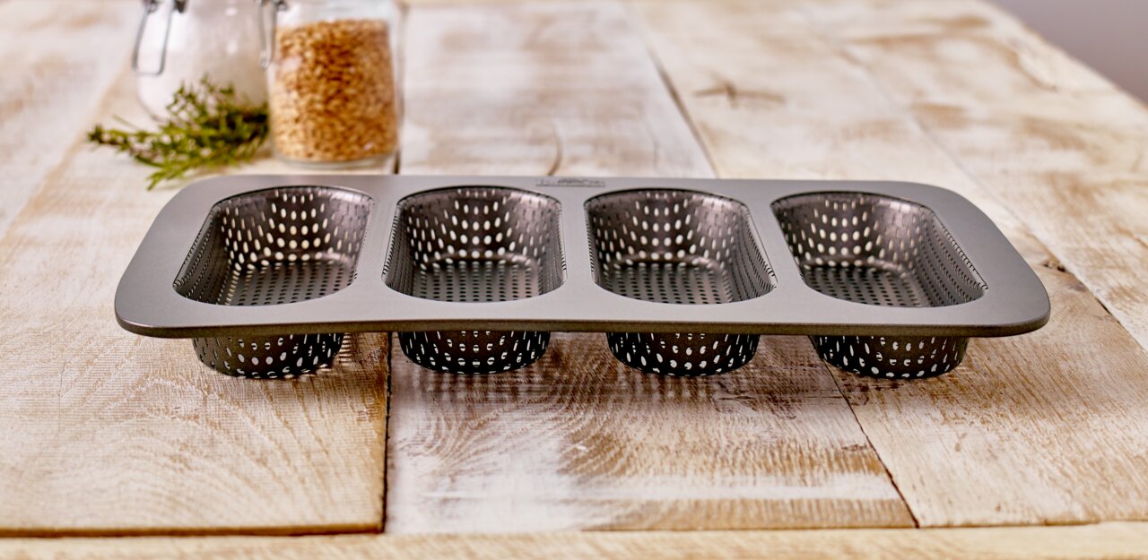 Hot Dog Brötchen-Blech mit vier perforierten Formen, seitliche Perspektive auf einem Holztisch