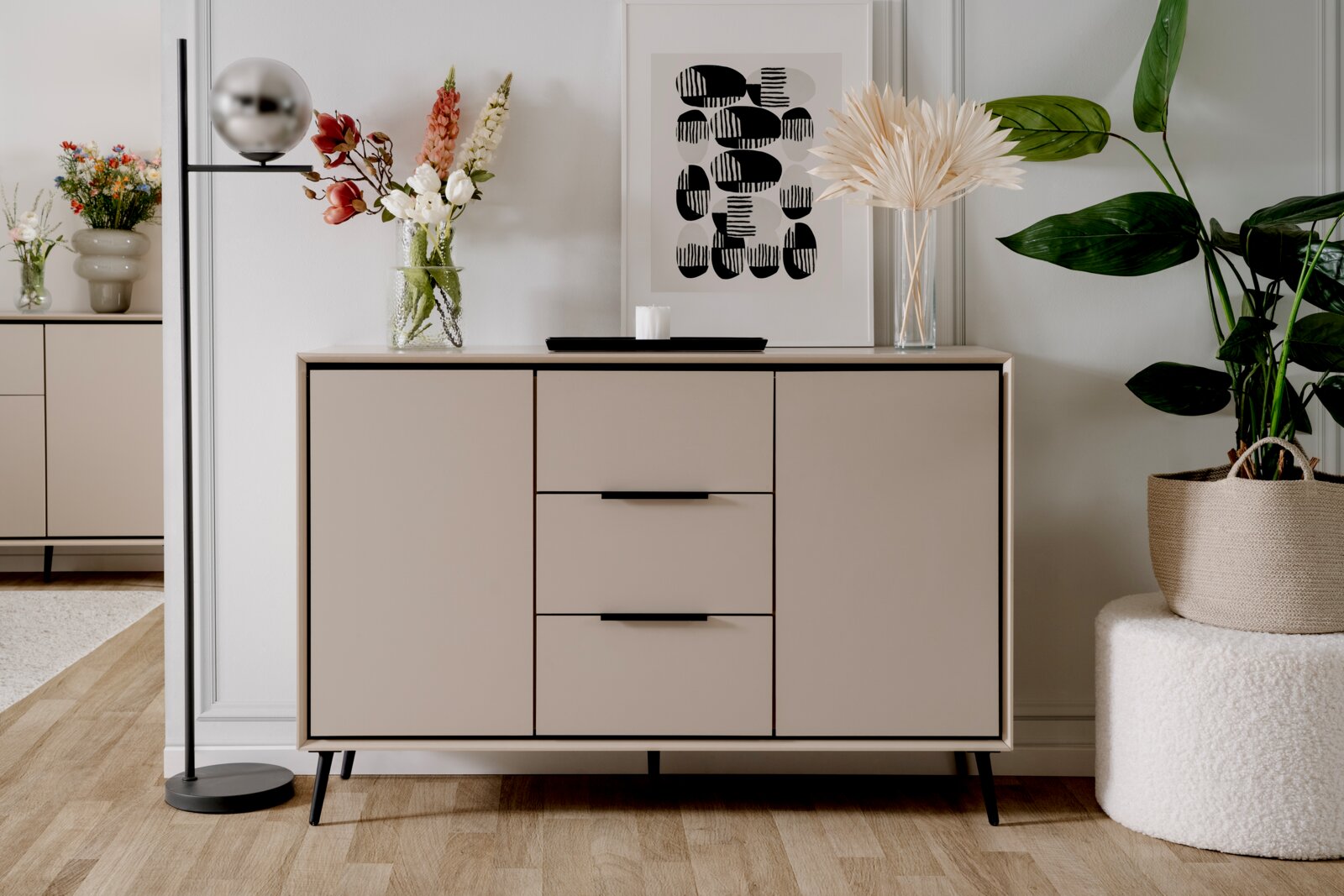 Z2 Dressoir ARONA Modernes Sideboard in neutralen Tönen mit drei Schubladen und zwei Türen, dekoriert mit Blumen und Kunstwerk, aus frontaler Perspektive.