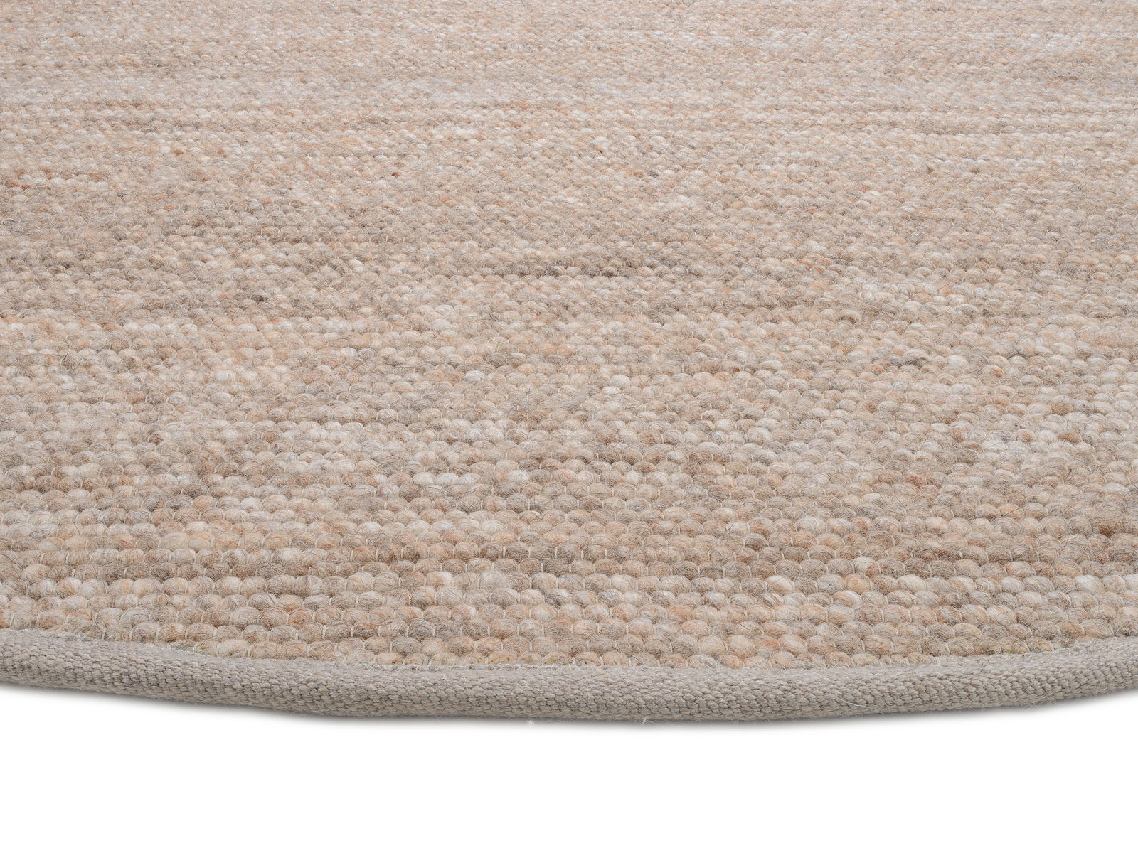 Nahaufnahme eines handgewebten Teppichs in natürlichen Beige- und Brauntönen, von der Seite fotografiert.