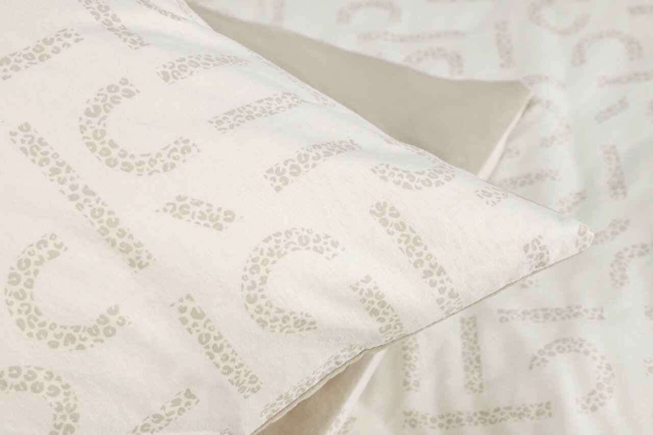 Nahaufnahme einer Bettwäsche mit dezentem Leopardenmuster in Beige auf weißem Hintergrund, perspektivisch von oben fotografiert.