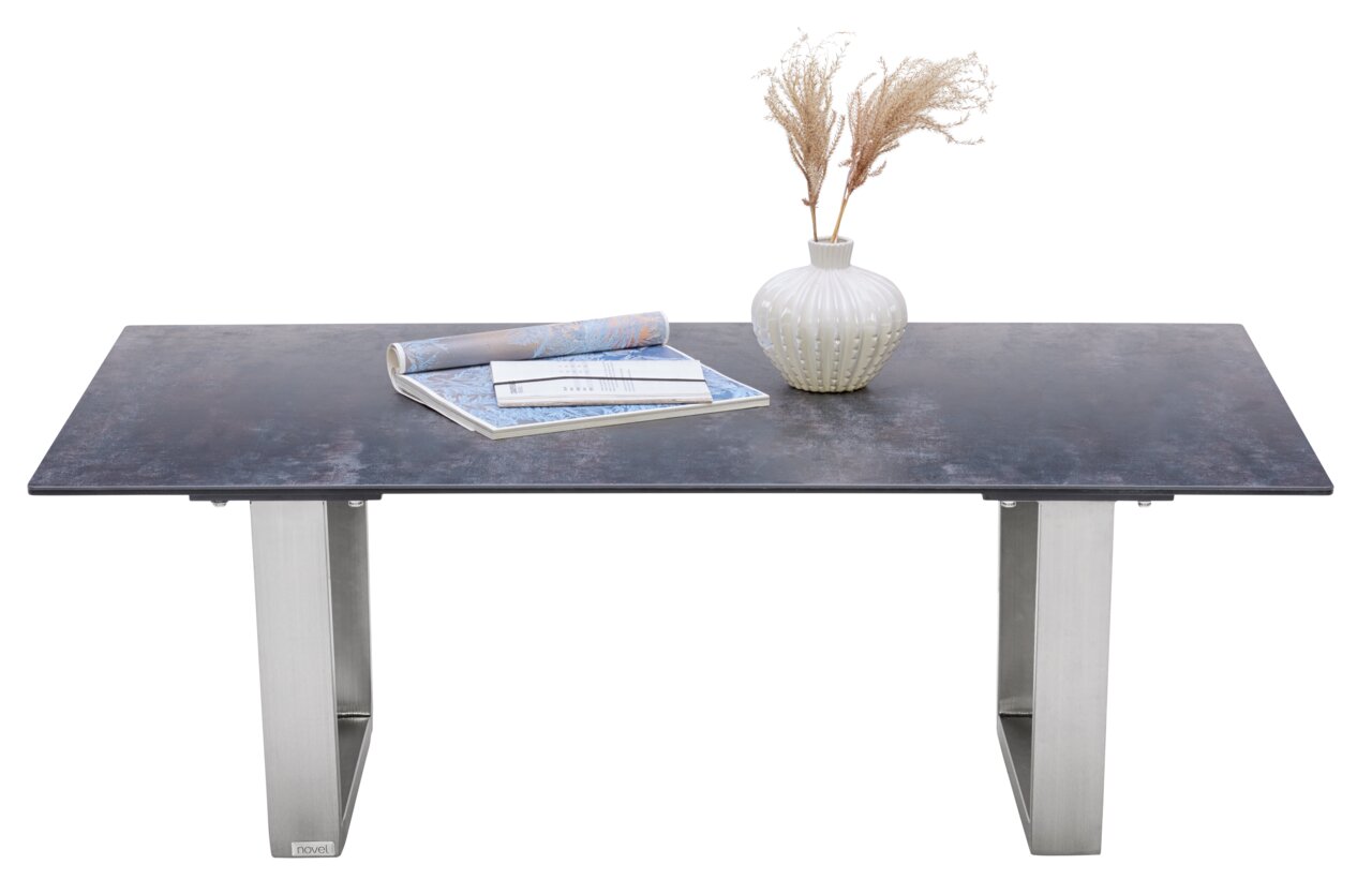 Moderner Couchtisch mit dunkler Tischplatte und silbernen Metallbeinen, dekoriert mit einer Vase und Zeitschriften, Frontalansicht.