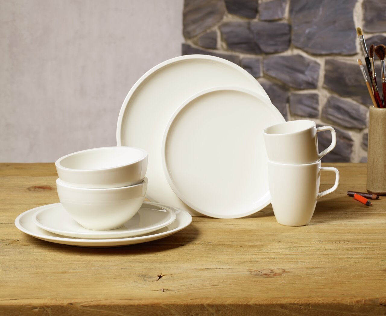 Startset van 8-delig wit porselein, bestaande uit borden, schalen en kopjes, op een houten tafel voor een stenen muur, zijaanzicht