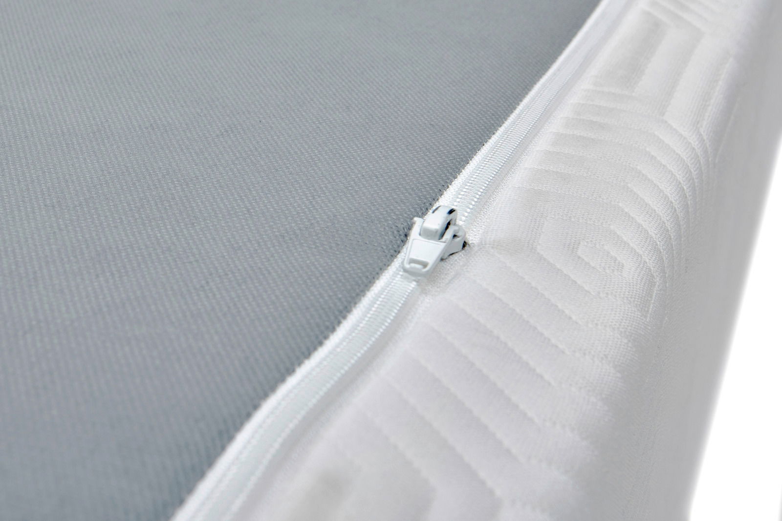 Nahaufnahme einer Viscomatratze mit grauer Oberfläche und weißem Reißverschluss an der Seite, perspektivisch von der Ecke aufgenommen.