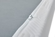 Close-up van een Viscoma-matras met een grijs oppervlak en een witte ritssluiting aan de zijkant, vanuit de hoek gefotografeerd.