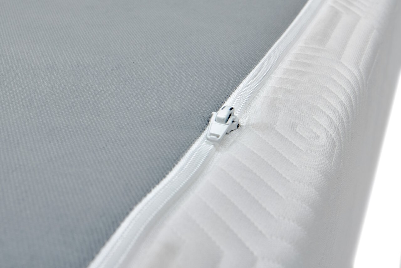 Close-up van een Viscoma-matras met een grijs oppervlak en een witte ritssluiting aan de zijkant, vanuit de hoek gefotografeerd.