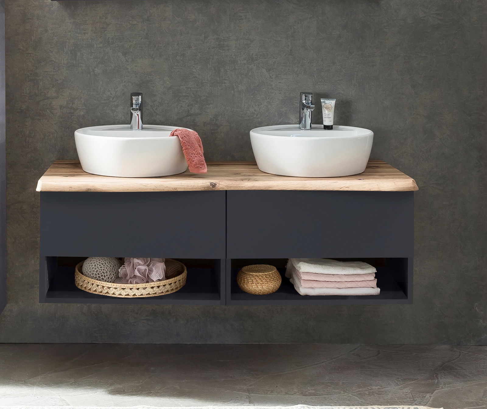 Frontale Ansicht eines modernen Waschtisch-Sets mit zwei runden Waschbecken auf einer Holzplatte, darunter dunkle Schubladen und offene Fächer mit Handtüchern und Körben.