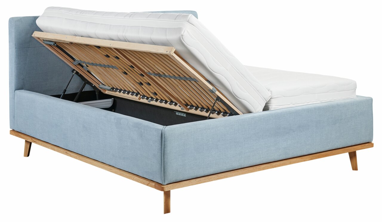 Gestoffeerd bed met lichtblauwe stoffen bekleding en houten poten, zijaanzicht met geopende opbergruimte