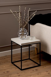 Moderner Couchtisch mit schwarzem Metallgestell und heller Holzplatte, seitliche Perspektive, dekoriert mit einer Glasvase und einem kleinen Glasobjekt.