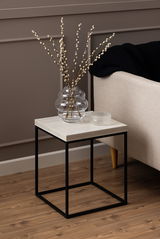 Moderner Couchtisch mit schwarzem Metallgestell und heller Holzplatte, seitliche Perspektive, dekoriert mit einer Glasvase und einem kleinen Glasobjekt.