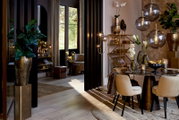 Eleganter Wohnraum mit modernen Möbeln und Dekorationen, darunter eine goldene Säule mit Pflanze im Vordergrund, aus seitlicher Perspektive betrachtet.