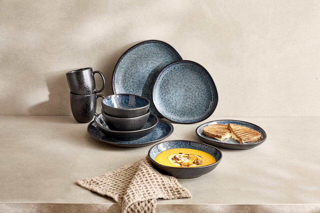 Kombiservice 10-teilig in dunklem Design mit blauen und grauen Tönen, bestehend aus Tellern, Schalen und Tassen, auf einer hellen Oberfläche arrangiert, seitliche Perspektive.