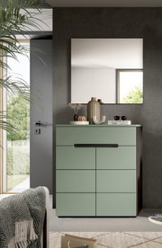 Modernes mintgrünes Sideboard/Kommode mit Schubladen und Türen unter einem rechteckigen Wandspiegel, dekoriert mit Vasen und Büchern, frontale Perspektive in einem minimalistischen Wohnraum