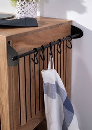 Nahaufnahme eines Servierwagens aus Holz mit schwarzen Haken an der Seite, an denen ein Geschirrtuch hängt. Perspektive von schräg oben.