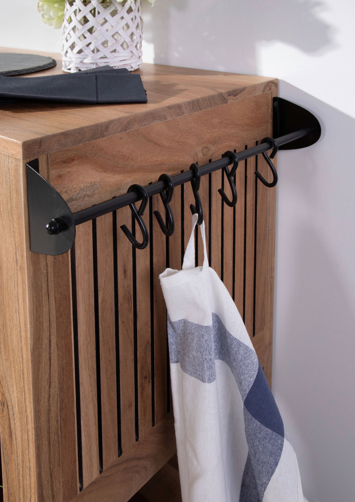 Nahaufnahme eines Servierwagens aus Holz mit schwarzen Haken an der Seite, an denen ein Geschirrtuch hängt. Perspektive von schräg oben.
