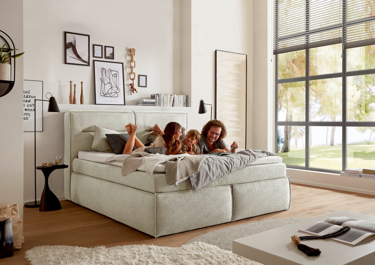 Gemütliches Boxspringbett in einem modernen Schlafzimmer, seitliche Perspektive, mit einer Familie, die darauf entspannt.