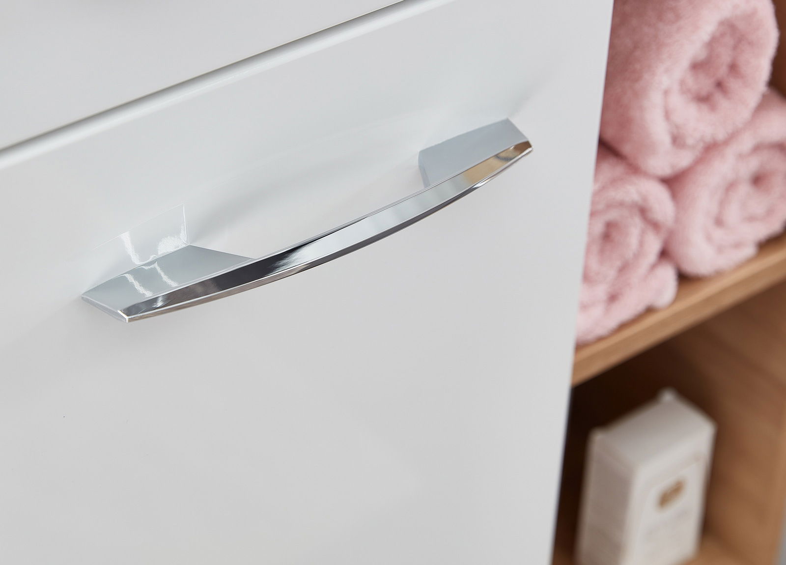 Nahaufnahme eines weißen Midischranks mit einem glänzenden, chromfarbenen Griff, seitliche Perspektive.