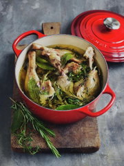 Roter Le Creuset Bräter, gefüllt mit Fleisch und Kräutern, auf einem Holzbrett von oben fotografiert.
