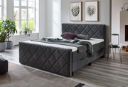 Graues Boxspringbett mit gestepptem Kopf- und Fußteil in einem modernen Schlafzimmer, seitliche Perspektive.