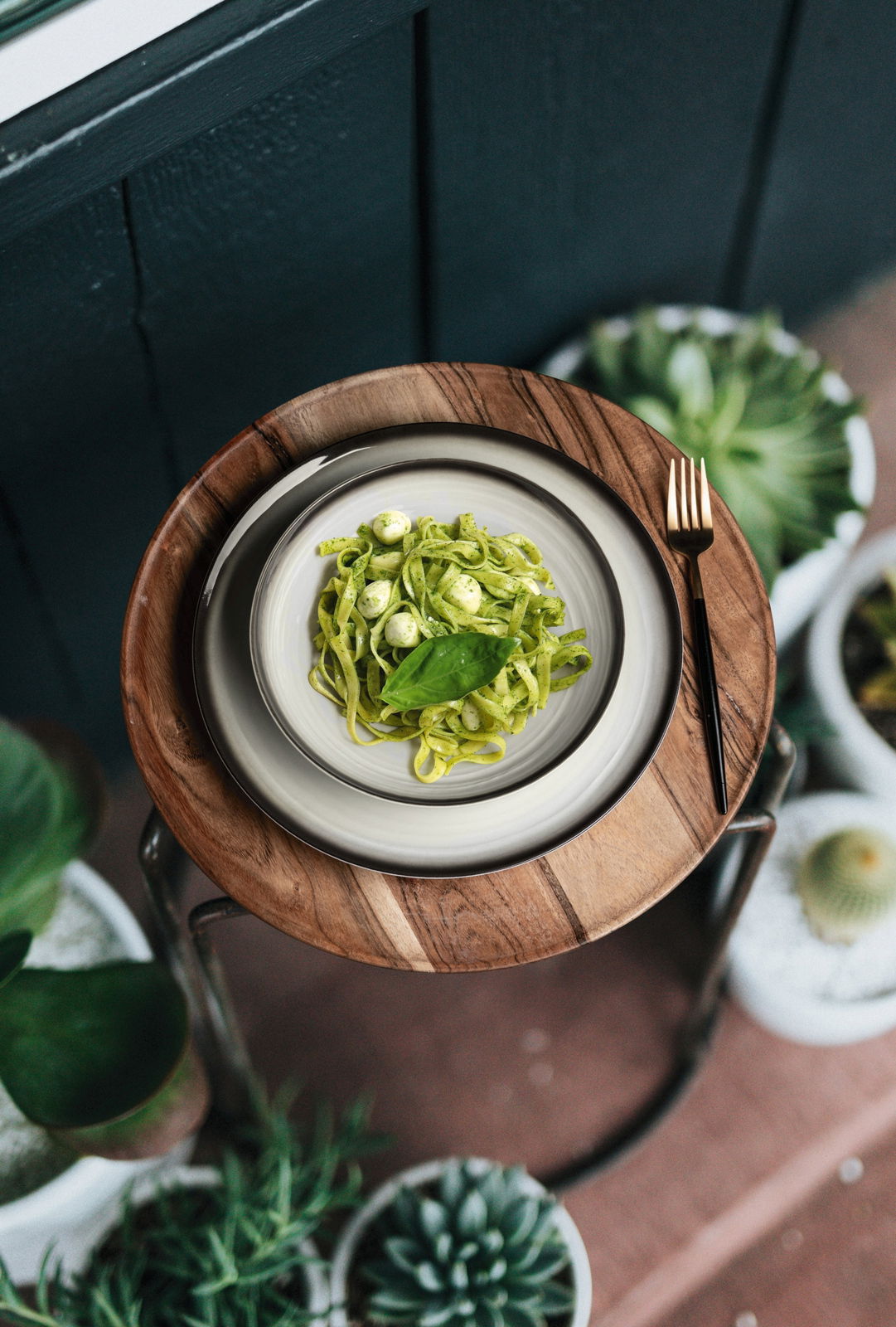 Vogelperspektive auf einen gedeckten Tisch mit einem Teller Pasta und einer Gabel, umgeben von Pflanzen.