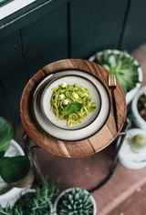 Vogelperspektive auf einen gedeckten Tisch mit einem Teller Pasta und einer Gabel, umgeben von Pflanzen.