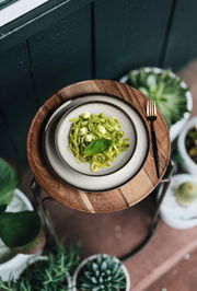 Vogelperspektive auf einen gedeckten Tisch mit einem Teller Pasta und einer Gabel, umgeben von Pflanzen.