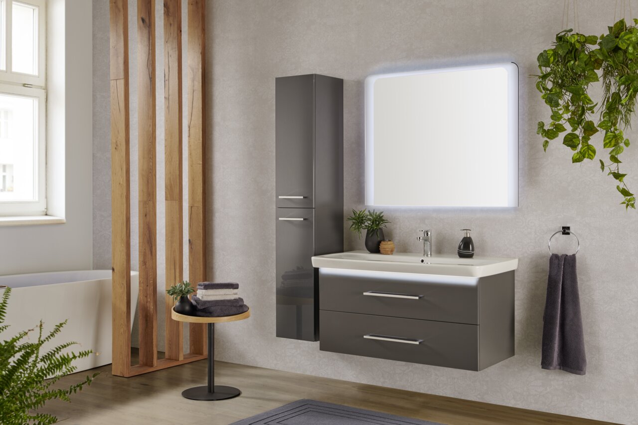 Modernes Badezimmer mit beleuchtetem Spiegelelement, grauem Waschtisch und hängenden Pflanzen, seitliche Perspektive.