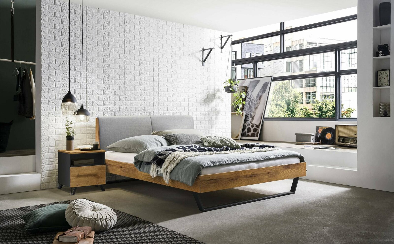 Modernes Bettgestell aus Holz mit grauem Kopfteil, seitlicher Blick in einem stilvoll eingerichteten Schlafzimmer mit großen Fenstern.