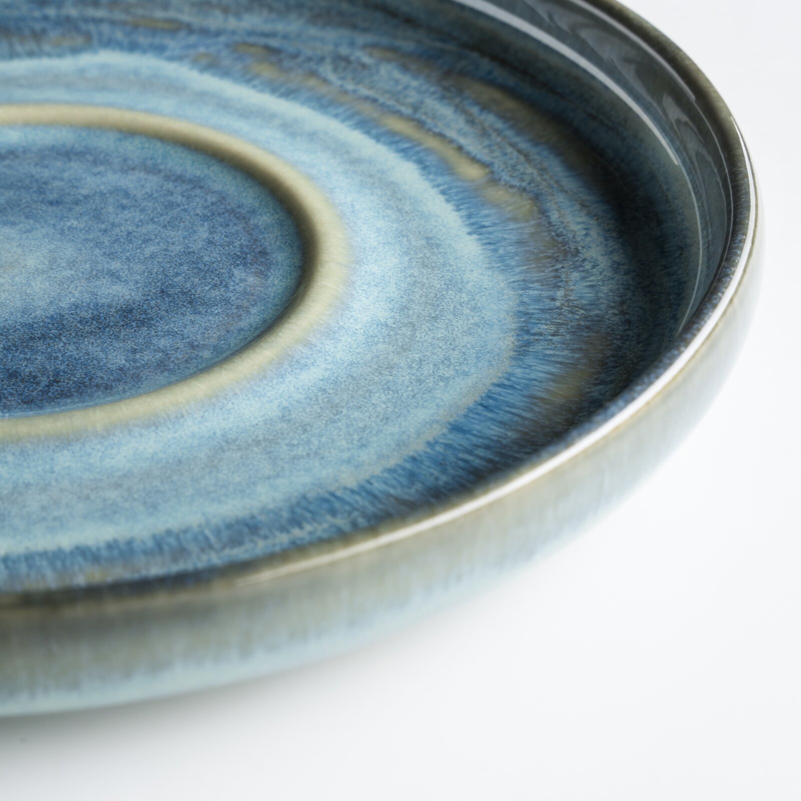Nahaufnahme eines glasierten Keramik-Tellers in Blau mit dezentem Ringmuster, schräg von oben fotografiert.