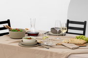Ein stilvoll gedeckter Tisch mit einem Weindekanter, gefüllt mit Rotwein, in der Mitte. Der Dekanter steht auf einem beigen Tischtuch, umgeben von Geschirr, Gläsern und einer Auswahl an Speisen. Die Perspektive zeigt den Tisch von der Seite.