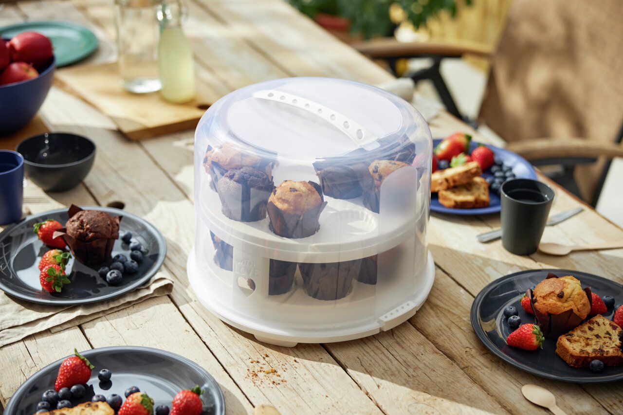 rotho Tortenglocke XL FRESH Tortenglocke XL 26 cm mit Tray, gefüllt mit Muffins, auf einem Holztisch im Freien, umgeben von Tellern mit Beeren und Gebäck, aus seitlicher Perspektive