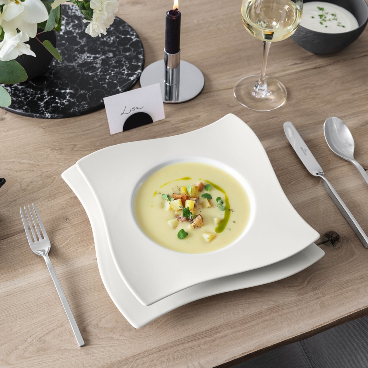 Suppenteller 24cm NewWave mit elegantem, wellenförmigem Design, von oben fotografiert, auf einem gedeckten Tisch mit Besteck und Weinglas.