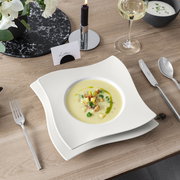 Suppenteller 24cm NewWave mit elegantem, wellenförmigem Design, von oben fotografiert, auf einem gedeckten Tisch mit Besteck und Weinglas.