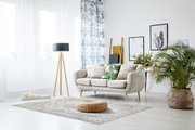Moderner Wohnraum mit hellem Sofa, dekorativen Kissen, Teppich in neutralen Tönen und Pflanzen, aus der Perspektive eines Betrachters im Raum.