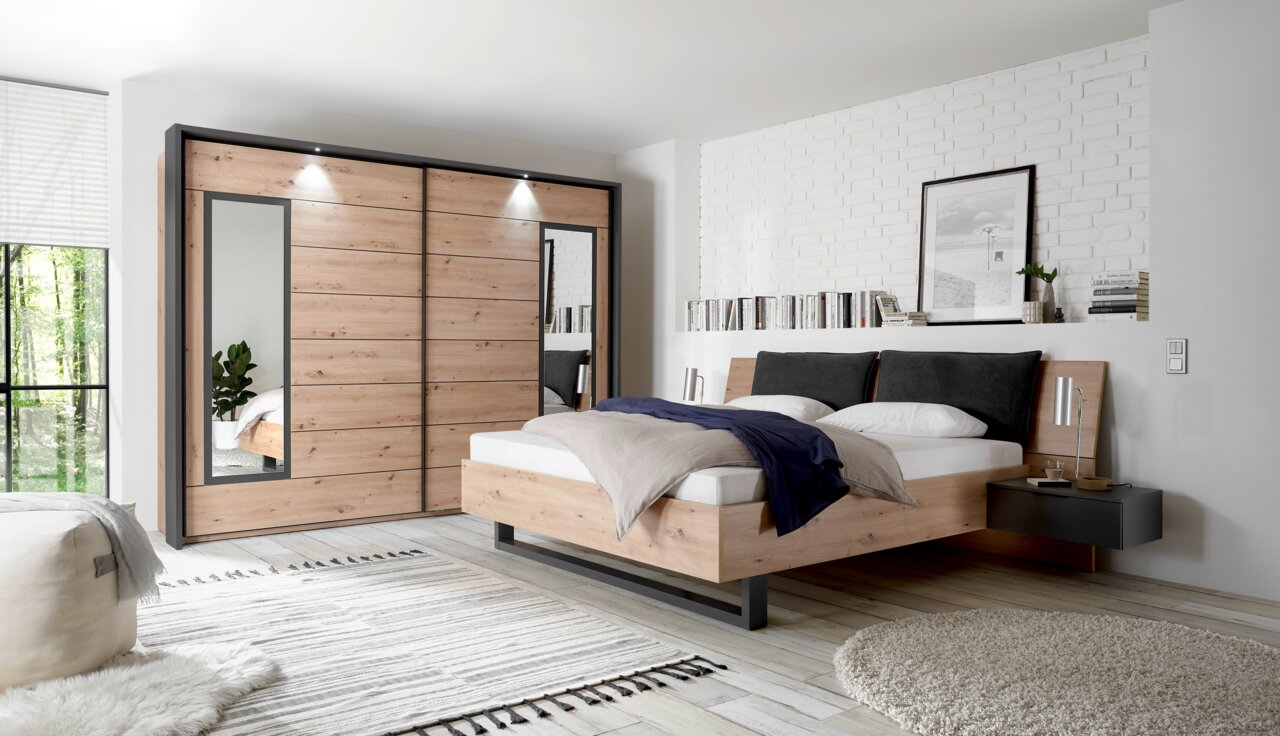 Moderne Schlafzimmermöbel mit einem Schwebetürenschrank und einer Bettanlage aus Holz in einer stilvollen, hellen Raumgestaltung, seitliche Perspektive.