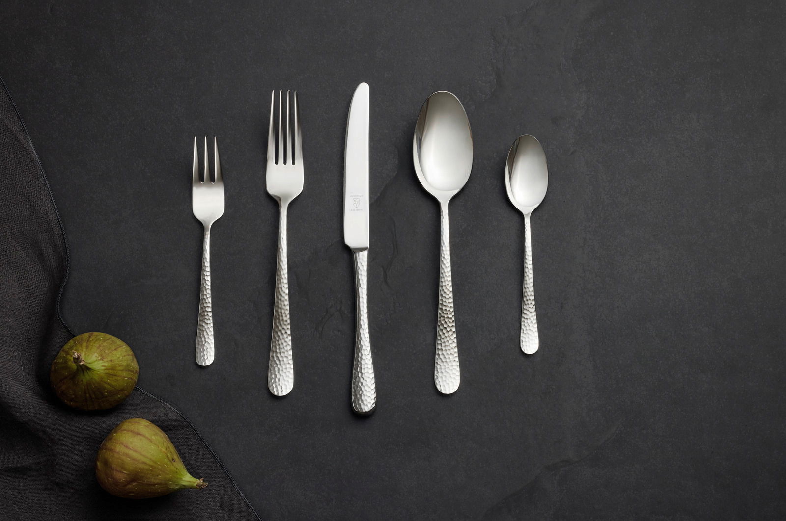 Justinus Besteck 60tlg. LOFTHOUSE Besteckset aus Edelstahl mit gehämmertem Griff, bestehend aus Gabel, Messer, Löffel und Teelöffel, auf dunklem Hintergrund von oben fotografiert.