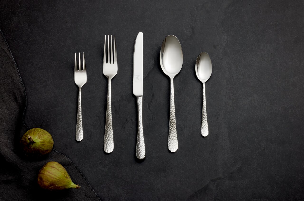 Justinus Besteck 60tlg. LOFTHOUSE Besteckset aus Edelstahl mit gehämmertem Griff, bestehend aus Gabel, Messer, Löffel und Teelöffel, auf dunklem Hintergrund von oben fotografiert.