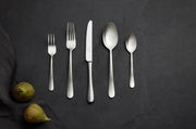 Besteckset aus Edelstahl mit gehämmertem Griff, bestehend aus Gabel, Messer, Löffel und Teelöffel, auf dunklem Hintergrund von oben fotografiert.