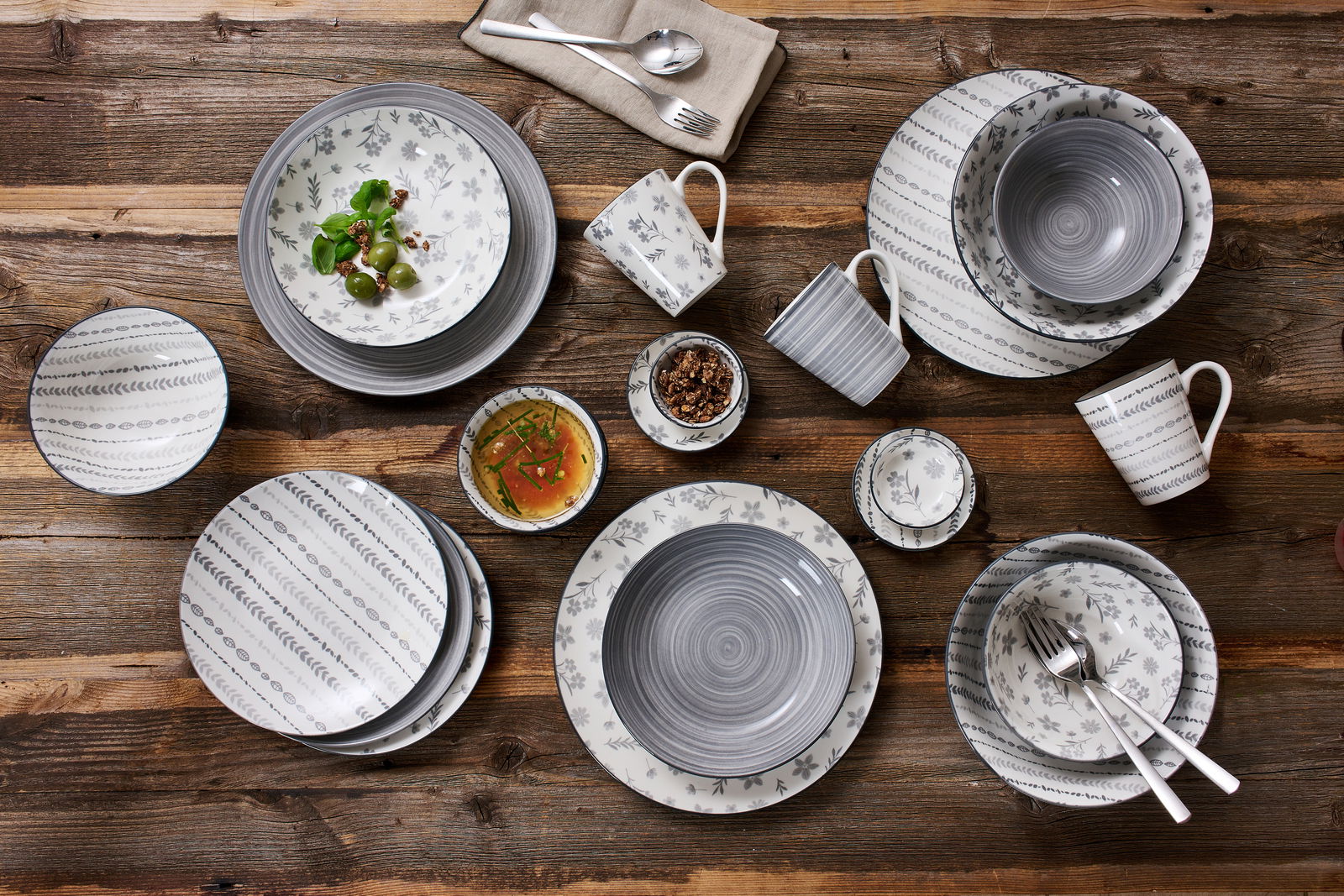 Vogelperspektive auf ein 16-teiliges Kombiset 'Sendai' mit grauen und weißen Mustern auf einem Holztisch.