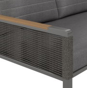 Detailfoto van een tweezitsbank met grijze stoffen bekleding, houten armleuningen en gevlochten zijkanten.