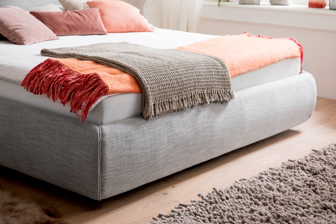 Graues Polsterbett mit dekorativen Kissen und Decken, seitliche Perspektive