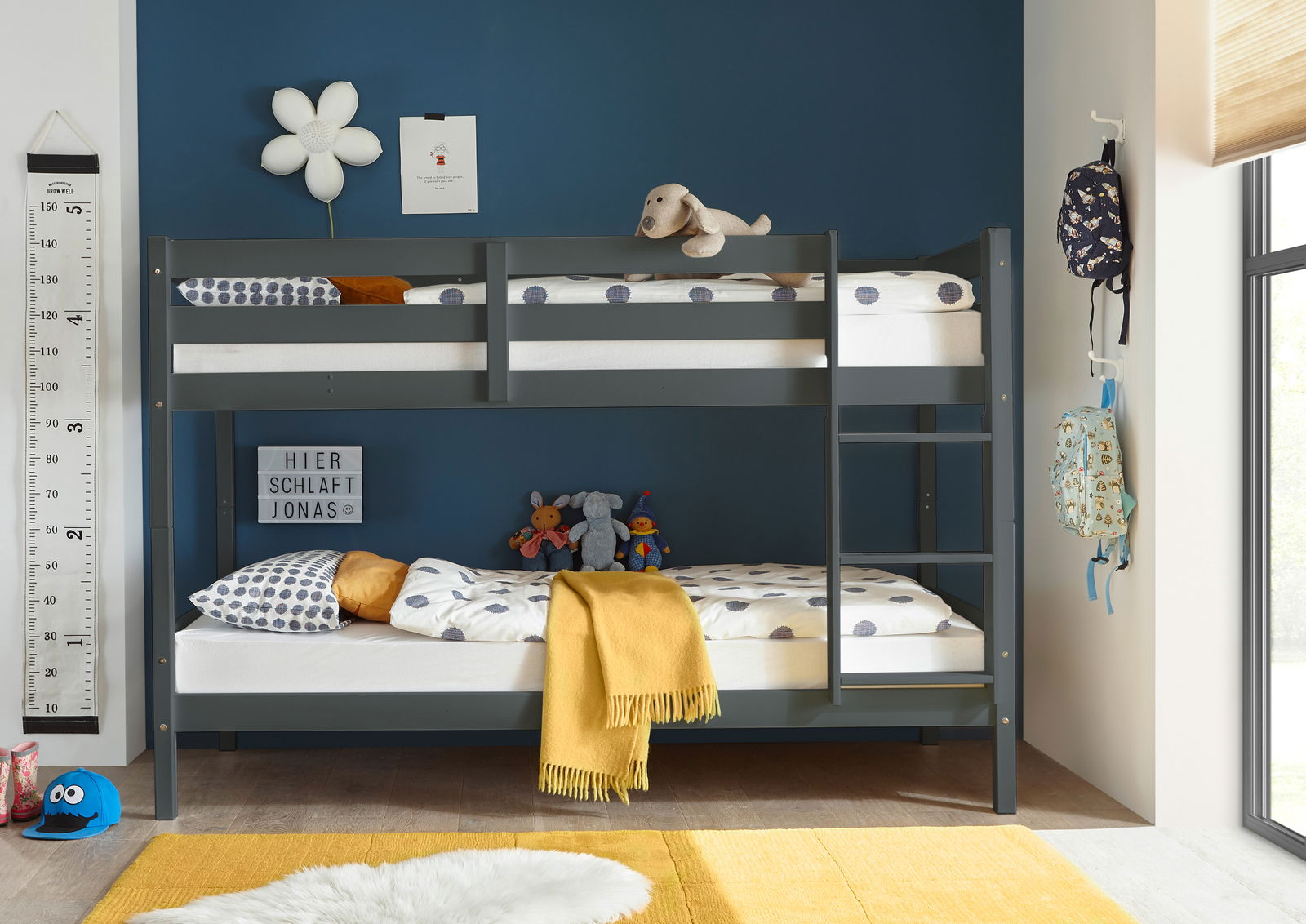Etagenbett in einem Kinderzimmer mit blauer Wand, dekoriert mit Kuscheltieren und bunten Kissen, seitliche Perspektive.