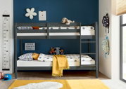 Stapelbed in een kinderkamer met een blauwe muur, versierd met knuffels en kleurrijke kussens, gezien vanaf de zijkant.