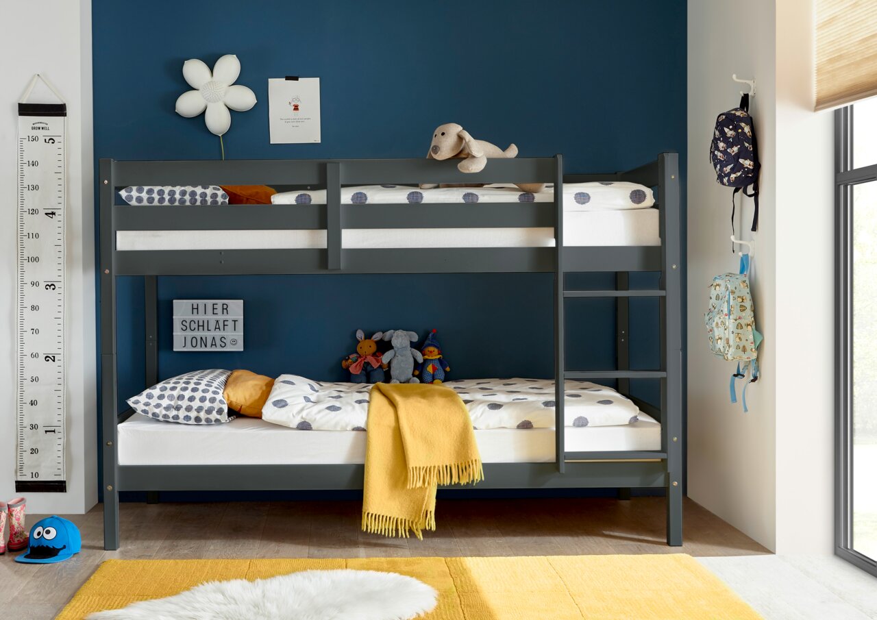 Stapelbed in een kinderkamer met een blauwe muur, versierd met knuffels en kleurrijke kussens, gezien vanaf de zijkant.